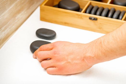 Hand of masseur takes black massage stones from the table in spa salon