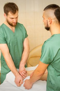 Two masseurs do foot massage in four hands for a female client in a spa salon