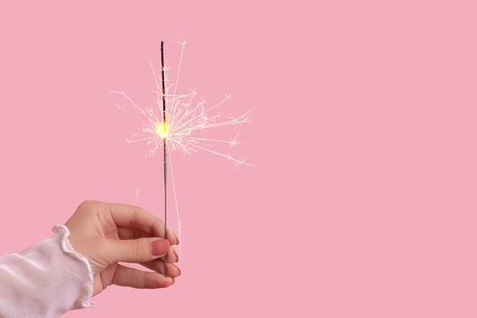 sparklers in a woman's hand on a pink background. Christmas holiday concept.