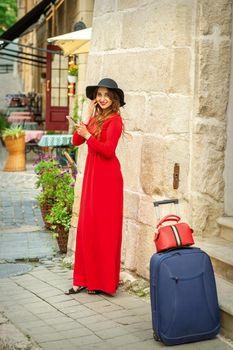 A young traveling white woman in the red jacket and black hat standing with a smartphone on the city street