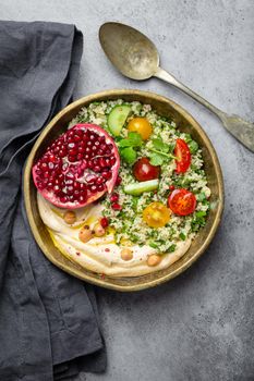 Rustic bowl with couscous salad with vegetables, hummus and fresh cut pomegranate. Middle eastern or Arab style meal with seasonings and fresh cilantro. Beautiful and healthy Mediterranean dinner .