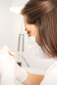 Manicure master in protective face mask and white gloves apply polish to female fingernails