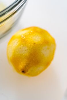 Zesting and juicing fresh lemon on a white cutting board.