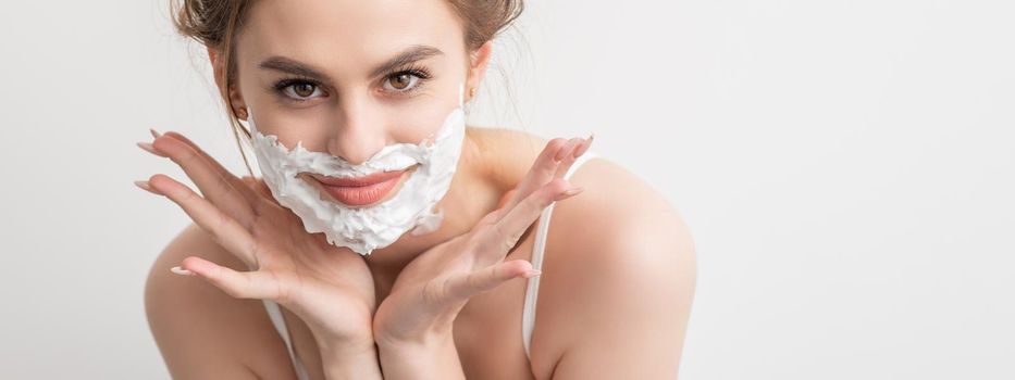 Portrait of a beautiful young smiling caucasian woman with shaving foam on face poses on white background