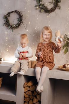 Little brother and sister play on Christmas eve in a beautiful house decorated for the New Year holidays. Children are playing with a Christmas gift. Scandinavian-style interior with live fir trees and a wooden staircase.