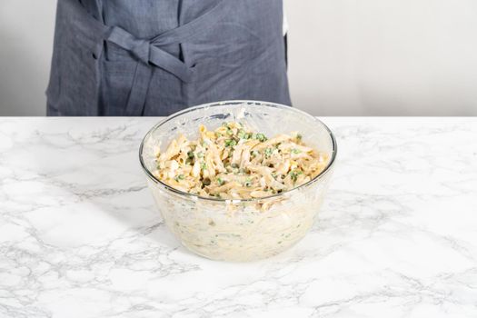 Mixing ingredients in a large glass mixing bowl to make macaroni salad with chicken.