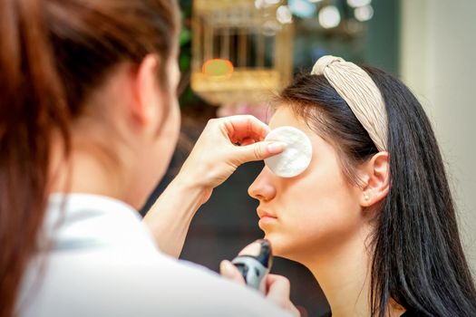 Makeup artist making professional makeup on the face of a young woman using an airbrush