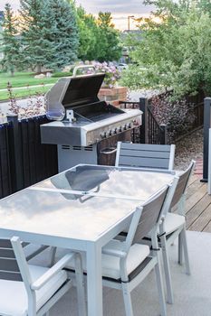 Morning on a summer day. Fully furnished backyard patio with a grill, sitting area, and umbrella.