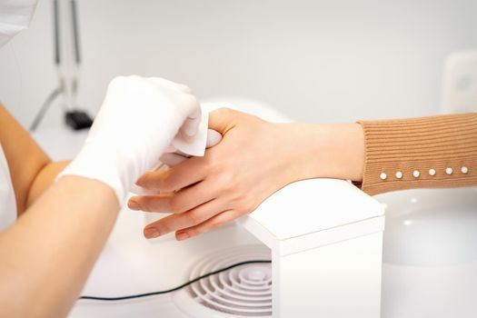 Hands of a manicurist in white protective gloves wipe female nails with a paper napkin in the salon