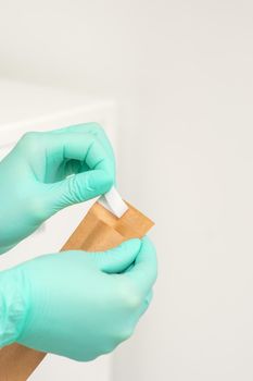 Beautician in green protective gloves holds a craft envelope to sterilize tools before disinfection