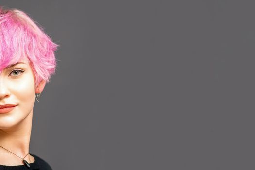 Portrait of beautiful young white woman with a pink short hairstyle on dark background with copy space