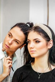 Make-up artist doing makeup for young beautiful bride applying wedding makeup in a beauty salon