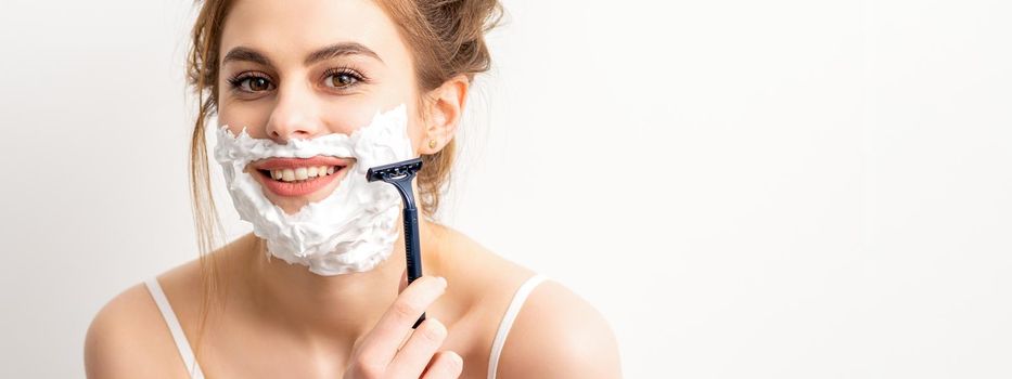 Portrait of beautiful young smiling caucasian woman shaves face with razor on white background