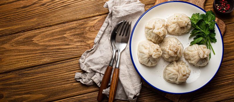 Khinkali, traditional dish of Georgian Caucasian cuisine, dumplings filled with ground meat on white plate with herbs on wooden rustic background table top view space for text.