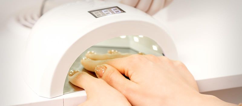 Female hand with manicured fingers dry inside UV light machine in manicure salon