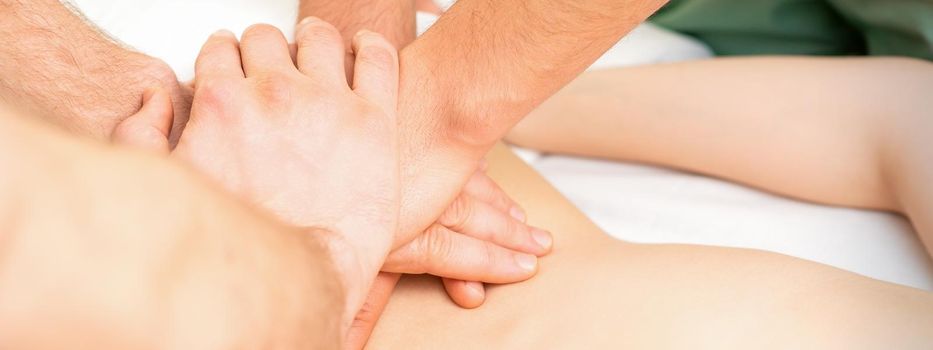 Young woman receiving a back massage in four hands by two masseurs at a spa salon