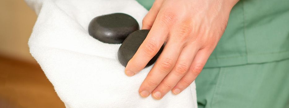 Close up of masseur's hand wipes black massage stones with a white towel