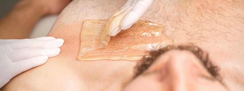 Young caucasian man receiving hair removal from his chest in a beauty salon, depilation men's torso