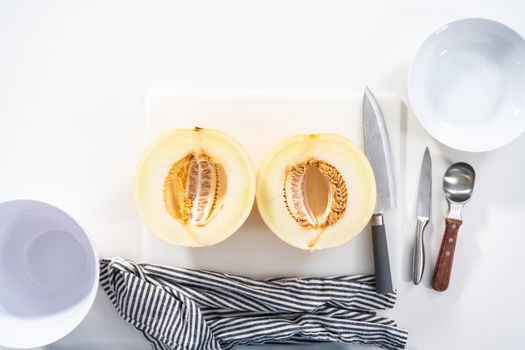 Flat lay. Slicong golden dewlicious melon on a white cutting board.