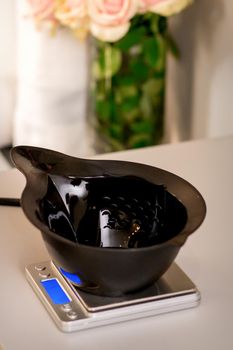 Black plastic empty bowl for hair coloring stands on electronic weight before mixing the hair dye