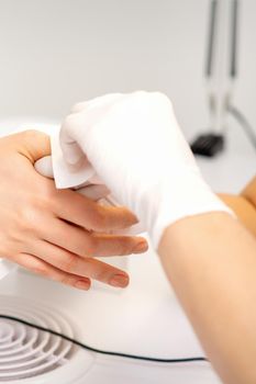 Hands of a manicurist in white protective gloves wipe female nails with a paper napkin in the salon