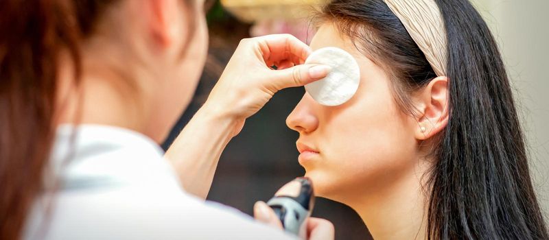 Makeup artist making professional makeup on the face of a young woman using an airbrush