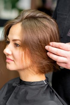 Male hairdresser works on the hairstyle of the young caucasian brunette woman at a hair salon