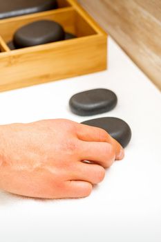 Hand of masseur takes black massage stones from the table in spa salon