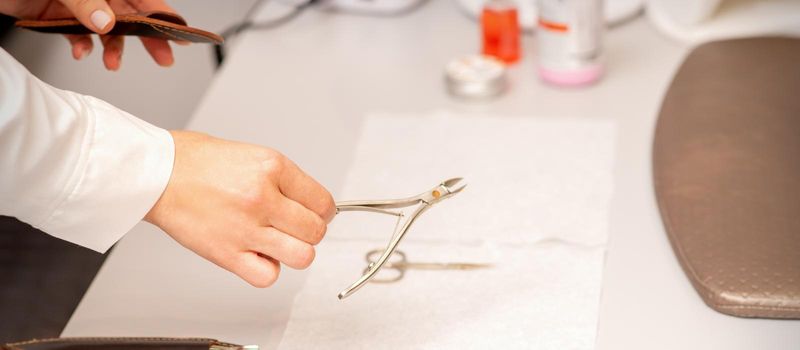 Nail nippers in the hand of female manicure master putting to the towel before nail care in manicure salon