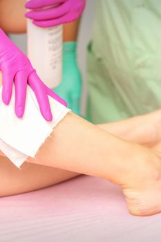 Master of depilation wipes female feet with white napkin preparing for the procedure of hair removal