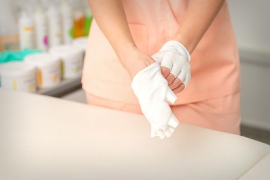 Cosmetologist in workwear wearing white bamboo fingerless gloves on her hands