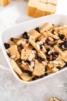 Baking bread pudding with raising and almond slivers in a white casserole dish.