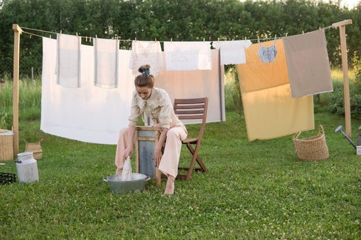 Laundry day. A woman hangs linen and towels on a tree in the courtyard of a village house. Summer cottage concept.