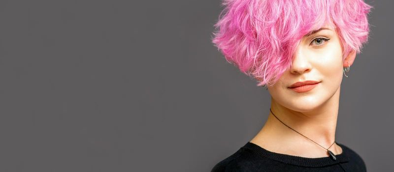 Portrait of beautiful young white woman with a pink short hairstyle on dark background with copy space
