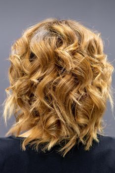 Back view of the woman with long brown curly hair stands on a dark background