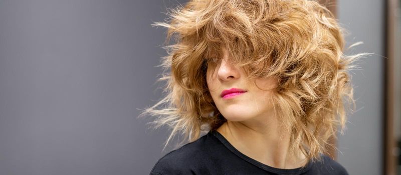 Portrait of beautiful young white woman with a curly light brown medium length hairstyle on dark background