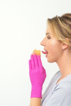 Young beautician licks liquid wax for depilation holding in gloved hands standing on white background. Cosmetologist tastes the sugar paste to taste