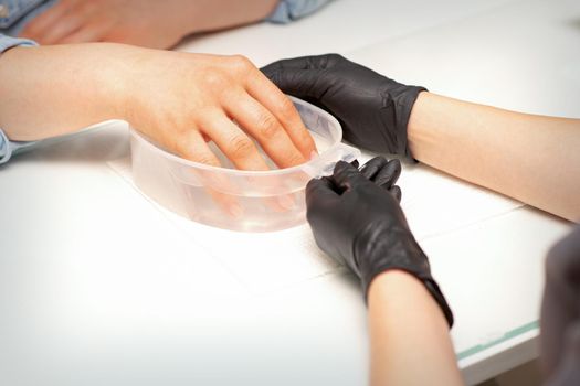The female dipped her hand in a bowl of water softening nails preparing for the manicure