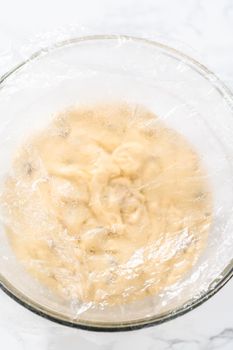 Rising dough in a glass mixing bowl to bake mini Easter bread kulich.