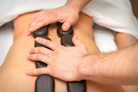Young caucasian woman receiving back massage with black stones by masseur in spa salon. A woman getting a spa treatment