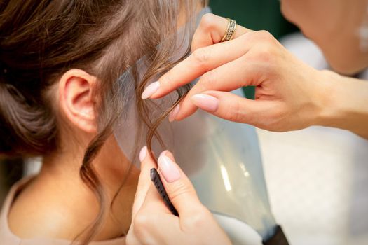 Close Up hairdresser stylist makes hairstyle for a young woman in a beauty salon