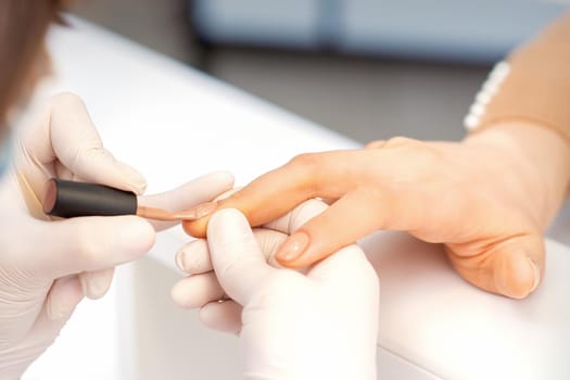 Hands of manicure master in white protective gloves apply polish to female fingernails