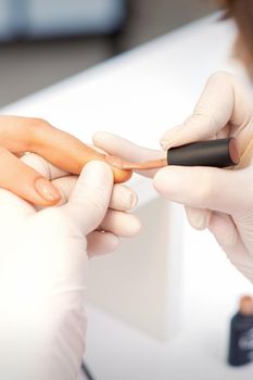 Hands of manicure master in white protective gloves apply polish to female fingernails