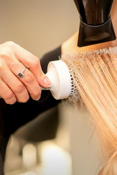 Professional hairdresser dry hair with a hairdryer and round hairbrush in a beauty salon