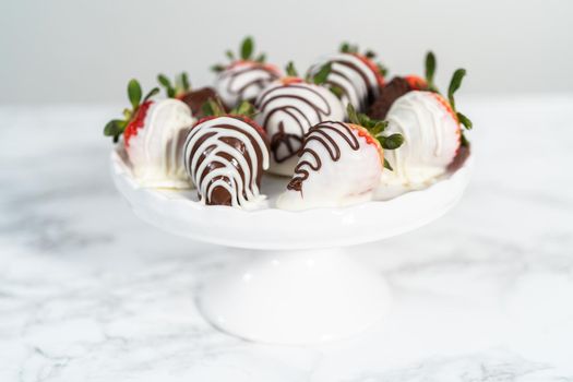 White and dark chocolate dipped strawberries on a white cake stand.