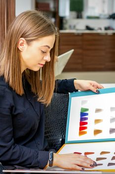 Young caucasian woman choosing a color from the hair color chart in a beauty salon