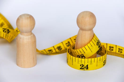Wooden doll wrapped with yellow measuring tape with customizable space for text or ideas. Copy space and weight loss concept.