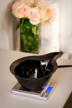 Black plastic empty bowl for hair coloring stands on electronic weight before mixing the hair dye