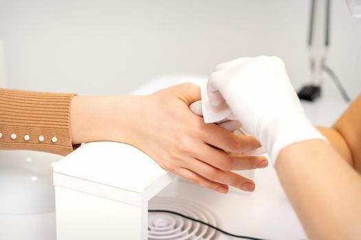 Hands of a manicurist in white protective gloves wipe female nails with a paper napkin in the salon