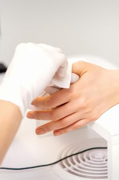 Hands of a manicurist in white protective gloves wipe female nails with a paper napkin in the salon